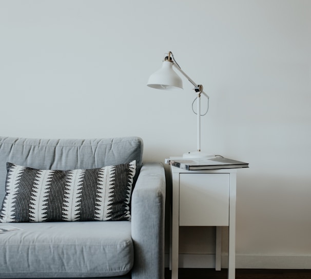 white study lamp on top of white wooden end table beside gray fabric sofa