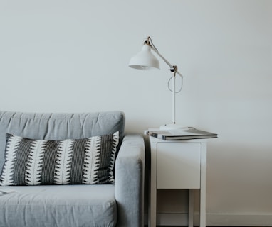white study lamp on top of white wooden end table beside gray fabric sofa
