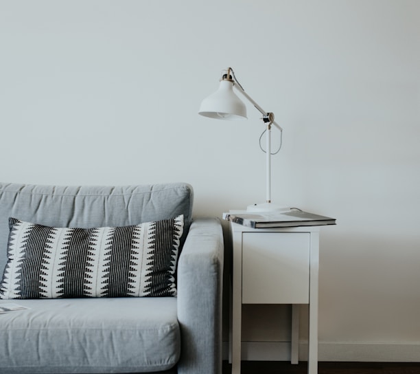 white study lamp on top of white wooden end table beside gray fabric sofa