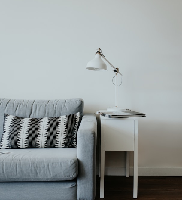 white study lamp on top of white wooden end table beside gray fabric sofa