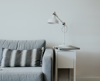 white study lamp on top of white wooden end table beside gray fabric sofa