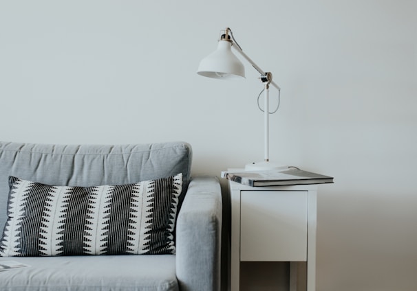 white study lamp on top of white wooden end table beside gray fabric sofa