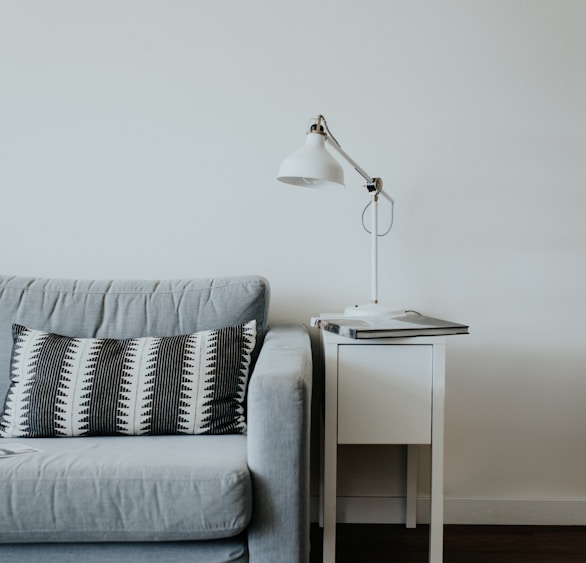 white study lamp on top of white wooden end table beside gray fabric sofa