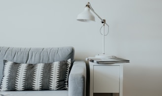 white study lamp on top of white wooden end table beside gray fabric sofa