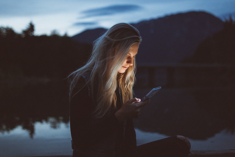 woman looking at phone beside body of water