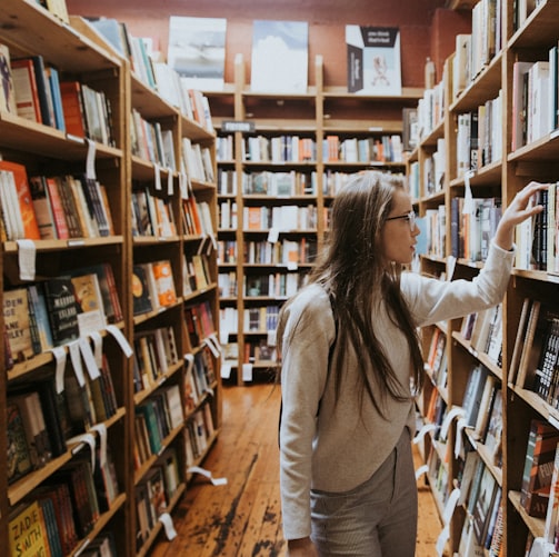 woman holding book on bookshelves