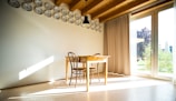A minimalist dining area featuring a light oak table and soft gray chairs bathed in natural light.
