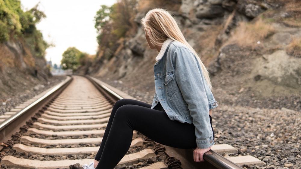woman in blue denim jacket and black leggings sitting on brown wooden bench during daytime