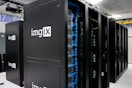 Several server racks with the logo 'imgIX' are neatly arranged in a data center. The racks are equipped with blue and yellow cable management, ensuring proper organization of the cables inside. The room is well-lit with overhead lighting and has a modern, clean appearance.