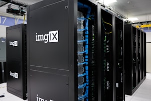 Several server racks with the logo 'imgIX' are neatly arranged in a data center. The racks are equipped with blue and yellow cable management, ensuring proper organization of the cables inside. The room is well-lit with overhead lighting and has a modern, clean appearance.