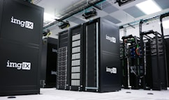A room filled with sleek black server racks, arranged neatly in rows. The servers are part of a data center with visible structured wiring and ceiling cable trays. Bright overhead lighting illuminates the space, adding to the modern high-tech environment.