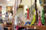Souvenir shop display with miniature Eiffel Tower replicas in various colors, including red, blue, green, and pink. The background shows shelves filled with other merchandise, blurred to emphasize the foreground objects.