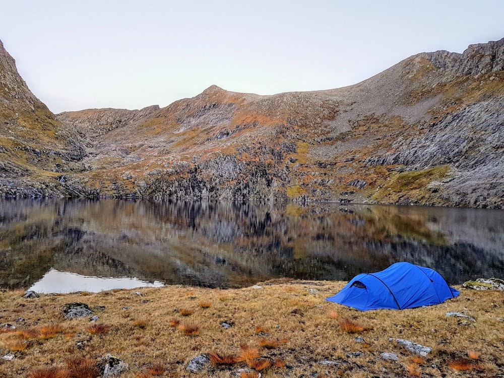 blue tent beside body of water surrounded by mountains during daytime