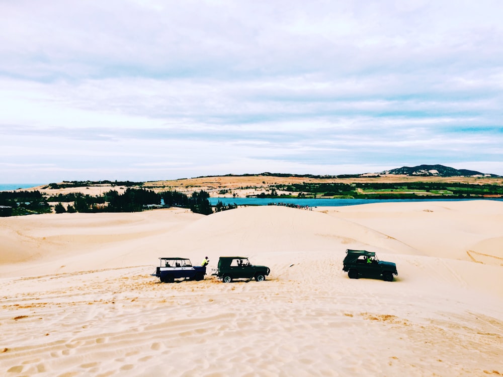 three off-road cars on white sand field during daytime