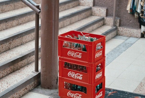 pile of four red Coca-Cola bottle crates near stairs
