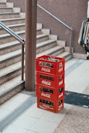 pile of four red Coca-Cola bottle crates near stairs