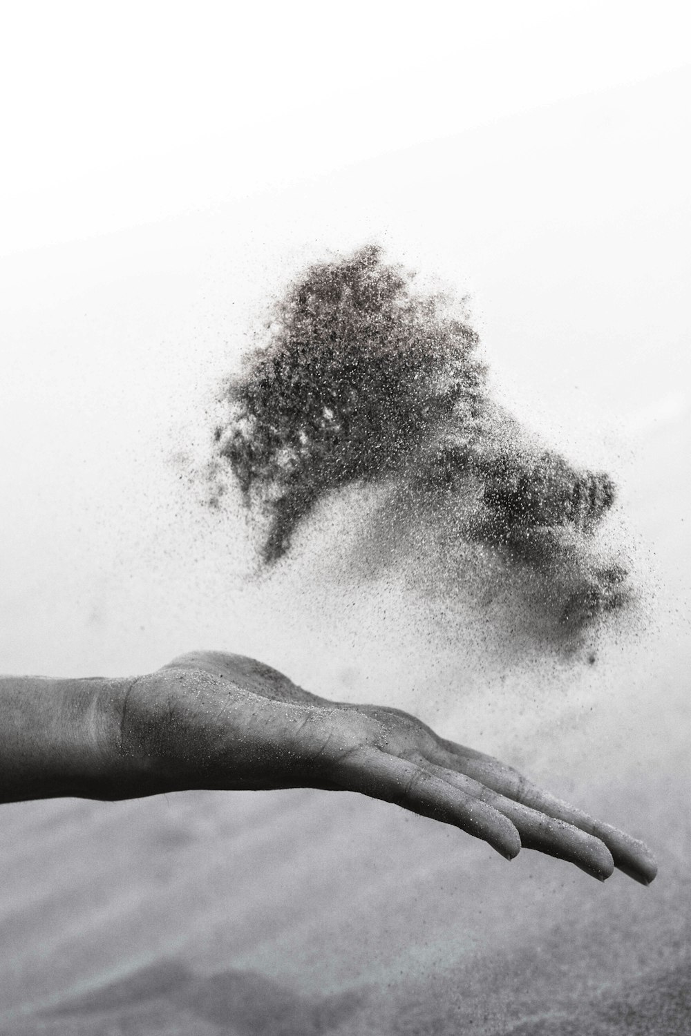 Fotografia in scala di grigi della mano della persona che sparge sabbia