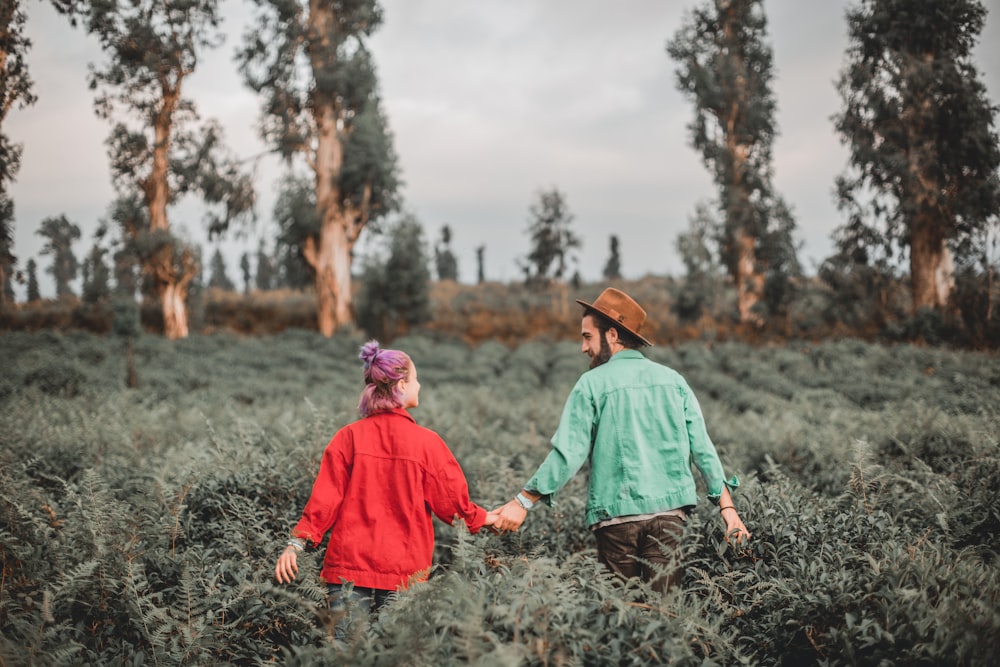 man and woman holding hands while walking on meadows