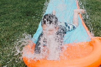 child sliding on blue and orange slippery pad with water splash at daytime