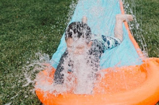 child sliding on blue and orange slippery pad with water splash at daytime