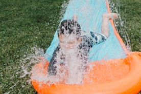 child sliding on blue and orange slippery pad with water splash at daytime