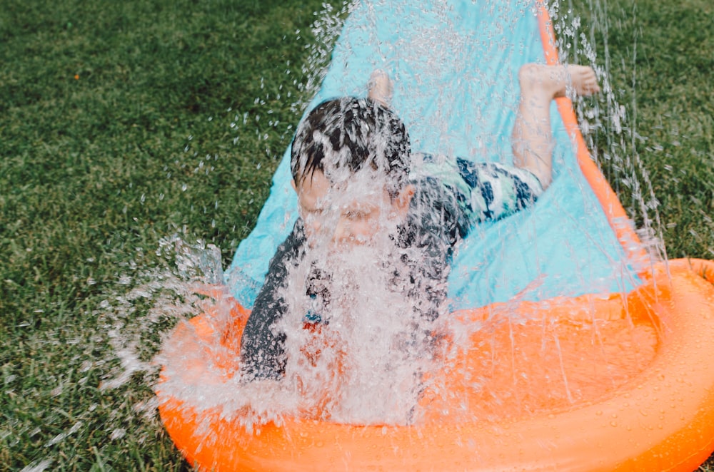 Enfant glissant sur un coussin glissant bleu et orange avec éclaboussures d’eau pendant la journée