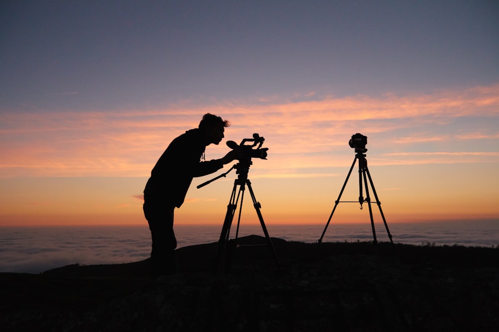 Silhouettenfoto einer Person, die die Kamera auf dem Stativständer draußen hält