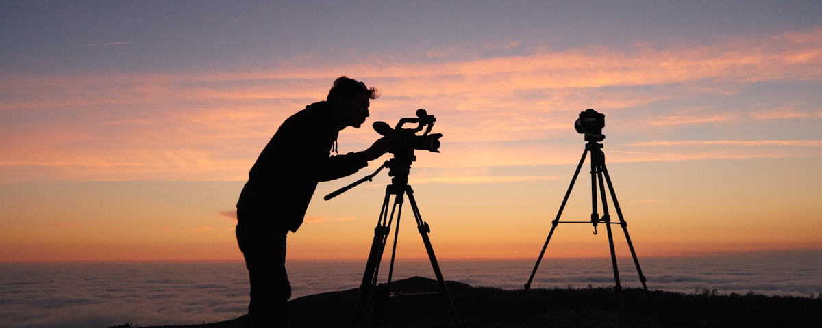 silhouette photo of person holding camera on tripod stand outside