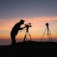 silhouette photo of person holding camera on tripod stand outside
