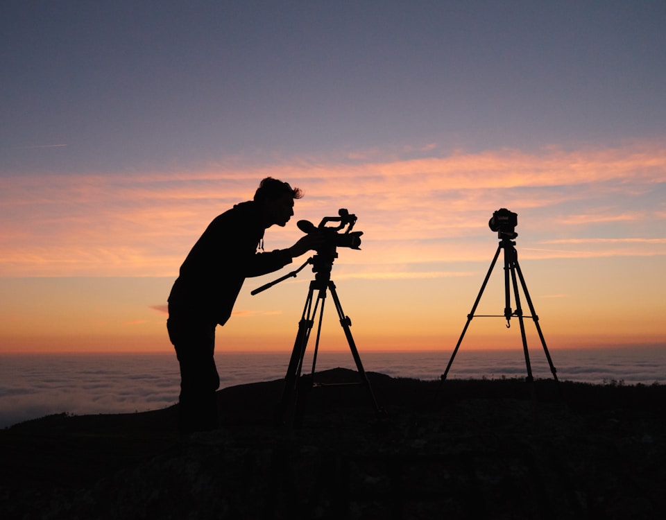 silhouette photo of person holding camera on tripod stand outside