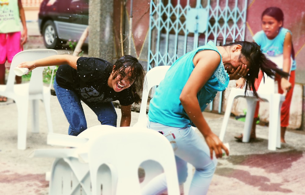 two woman playing with water near plastic chairs