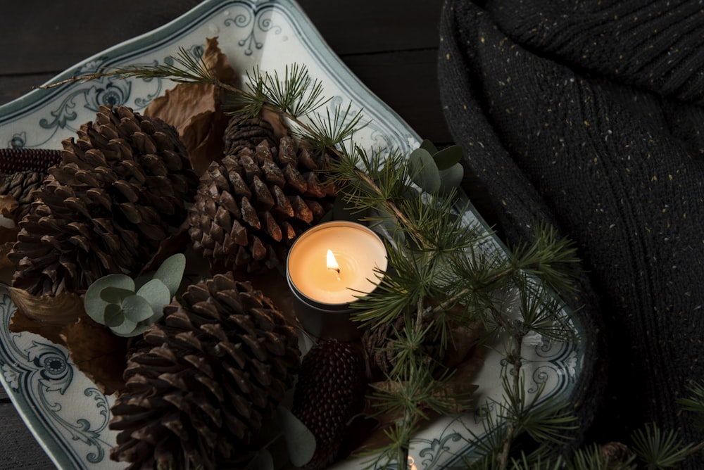 lighted candle on plate beside the pinecones
