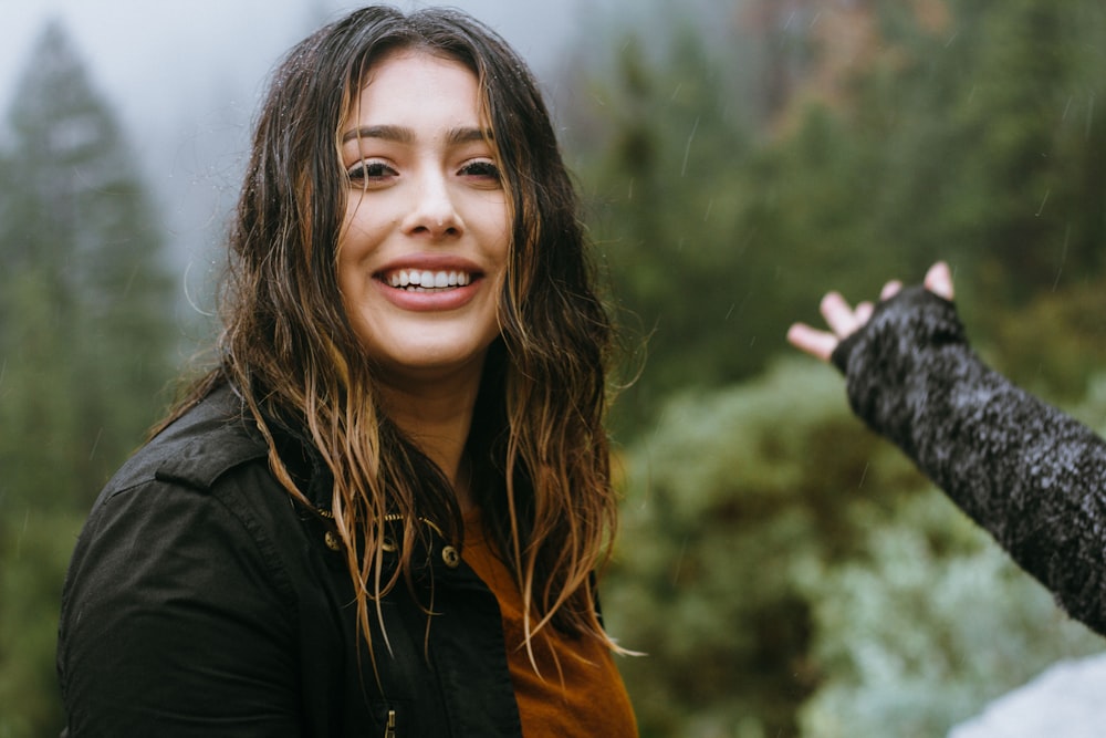 femme portant une veste noire souriant avec un fond de forêt