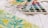 A palette of watercolors with various shades is resting on a white surface next to a floral watercolor painting featuring green leaves and yellow flowers.