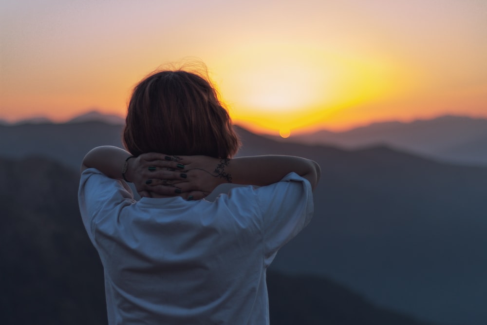 woman facing backward holding head facing sunset