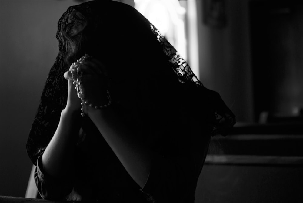 fotografia in scala di grigi di una donna che prega mentre tiene in mano i rosari