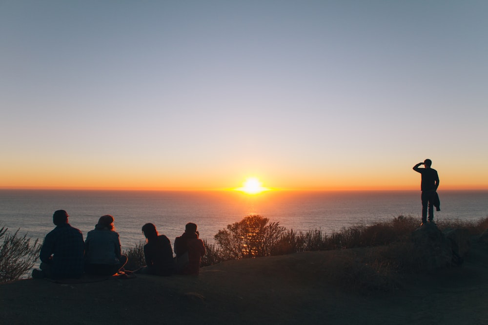 silhouette di persone sedute e in piedi sulla collina vicino all'oceano all'ora d'oro