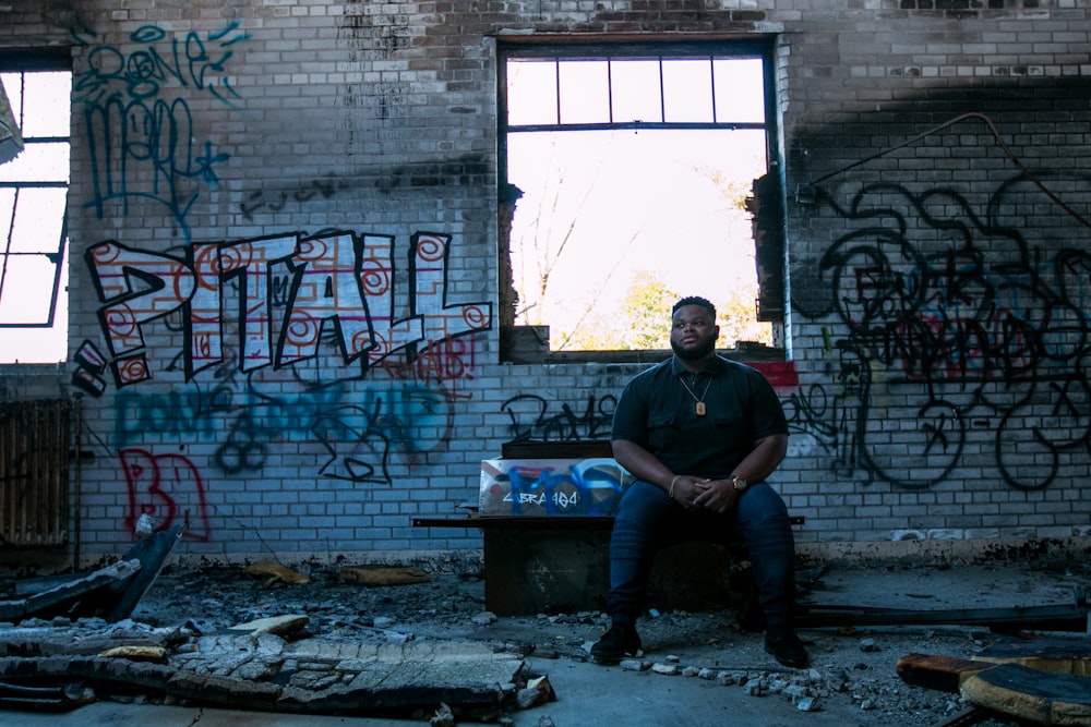 man sitting on bench front of assorted-design graffiti on wall