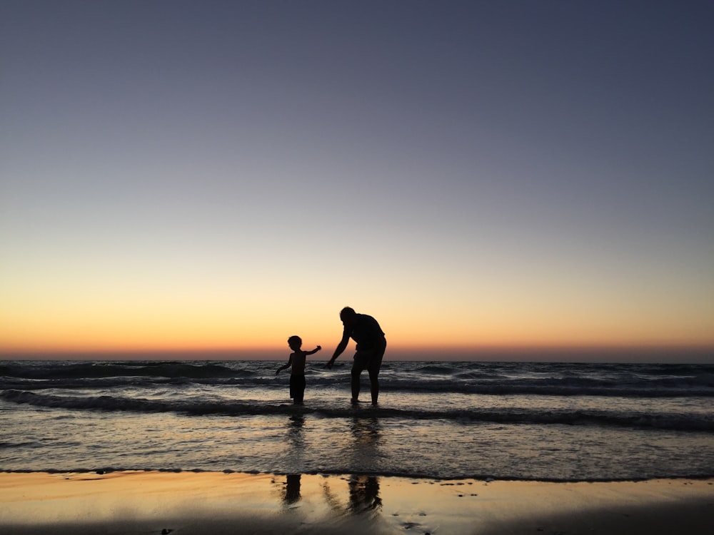 silhouette of man and kid on seashore