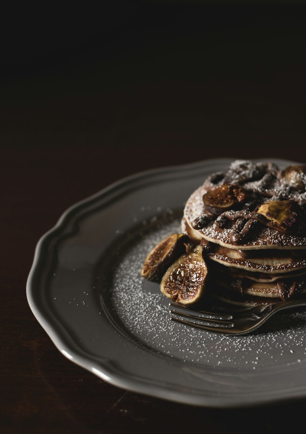 Fotografia de foco raso de pan cakes com fatias de banana e xarope por cima em prato cinza