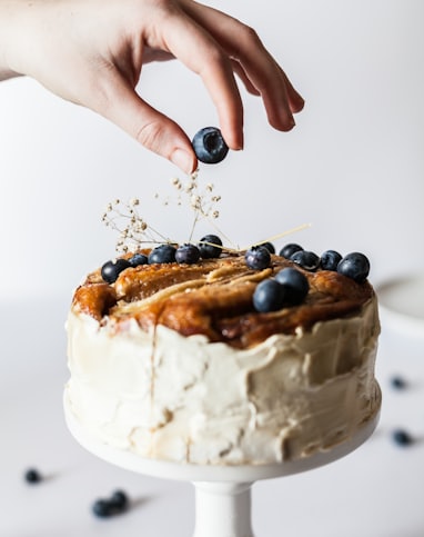 person holding black fruit near cake