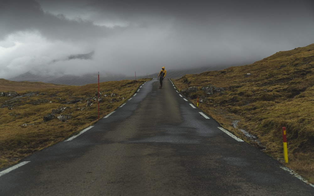 person walking on concrete road between grass fields