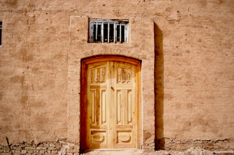 A beautifully crafted wooden door with intricate Baja-style carvings, set against a vibrant stucco wall.