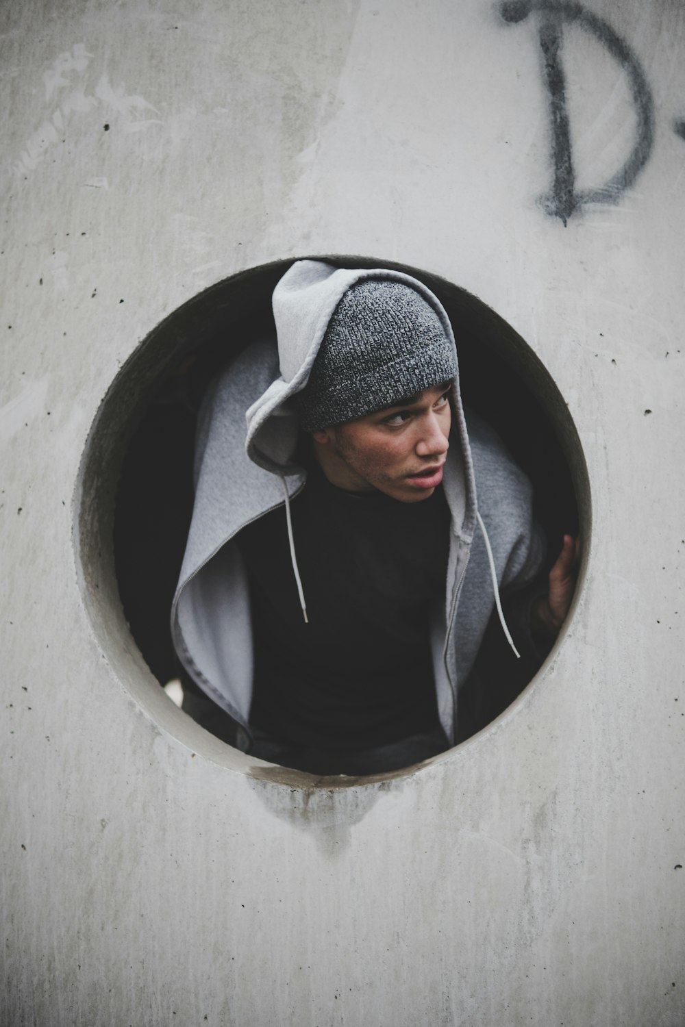 man wearing black shirt and knit cap with hoodie jacket inside concrete hole