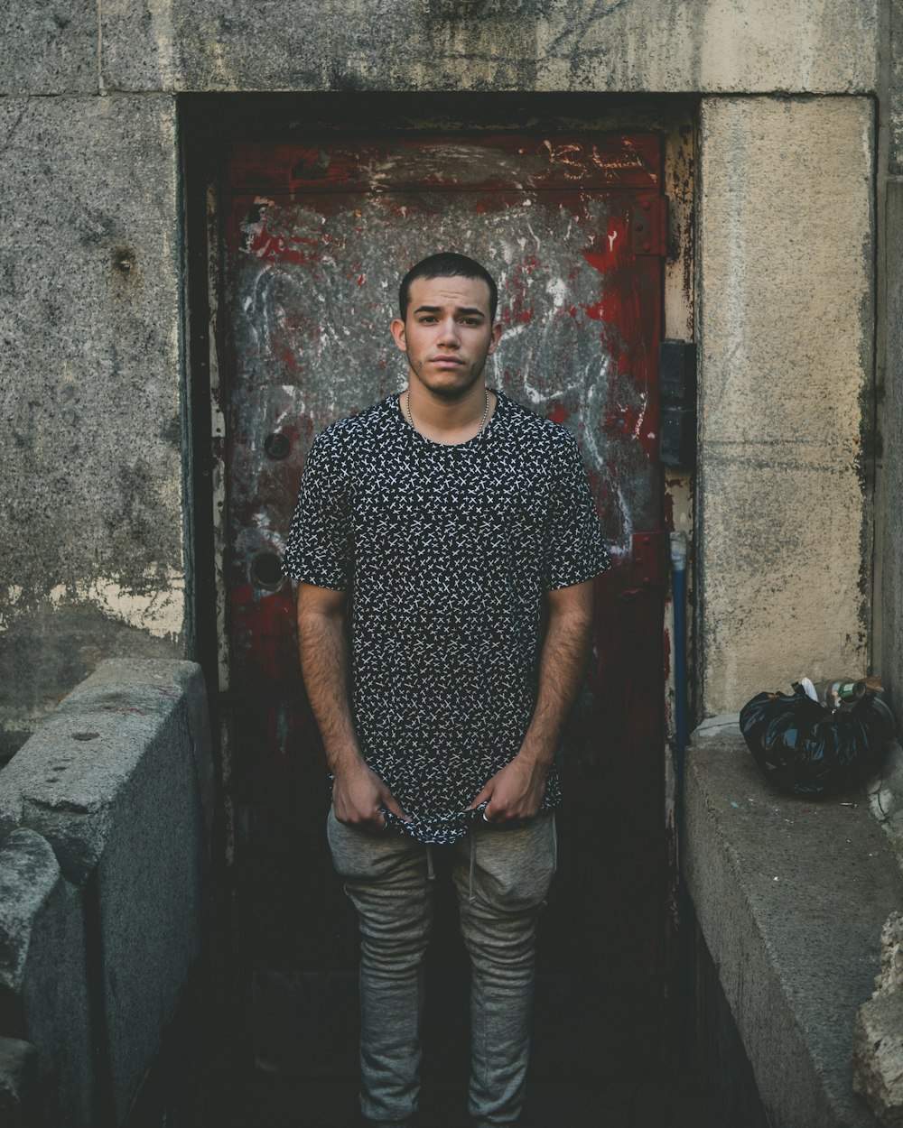 man standing while holding on to his black top near red door