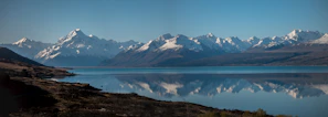 A panoramic view of snow-capped peaks reflected in a crystal-clear alpine lake on a bright day