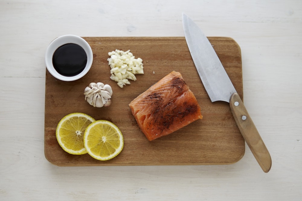 graues Messer und orangefarbenes Fleischfleisch auf Holzschneidebrett