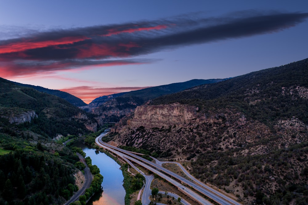 aerial photography of concrete road near river and mountain during sunset