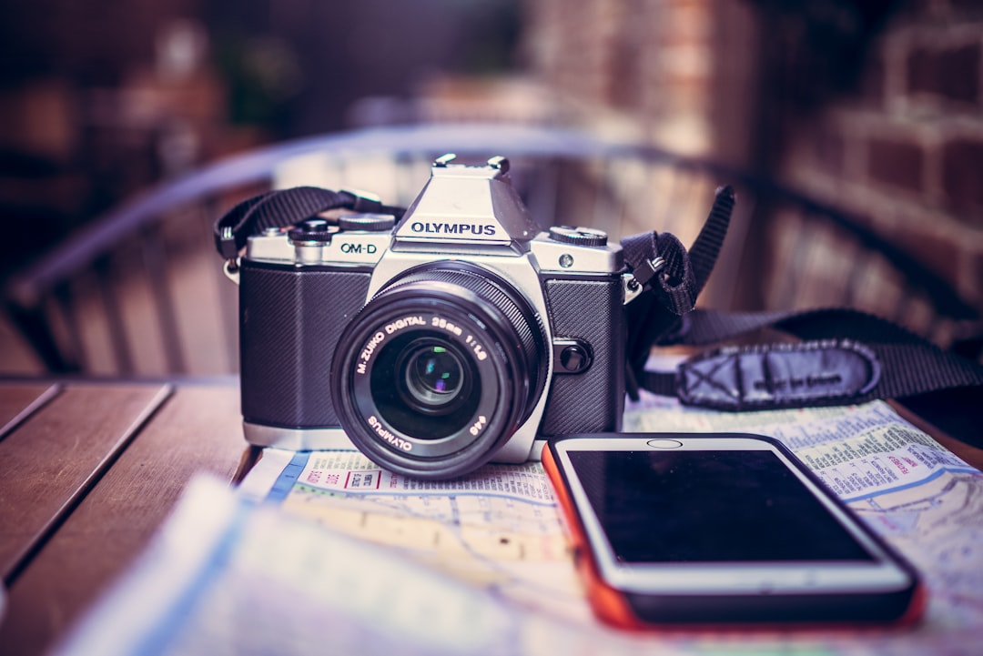 black Olympus SLR camera near white iPhone, Camera. Coffee. iPhone. Map. Go.