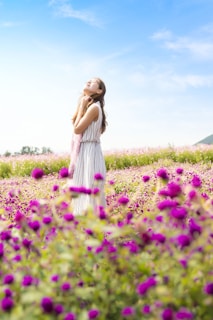 woman wearing white and gray striped sleeveless dress smelling the air standing in the pink flower field at daytime
